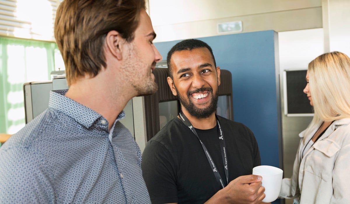 Två unga män som pratar och skrattar vid en kaffemaskin.