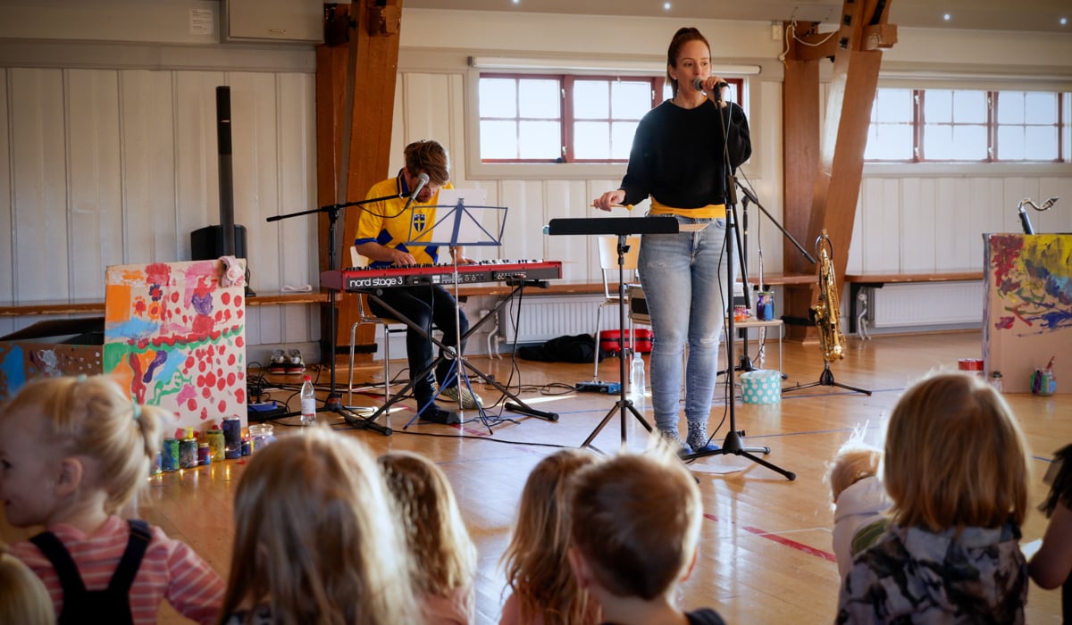 Två musiker, en sjunger och den andra spelar på en keyboard. Framför dem syns barn som lyssnar.