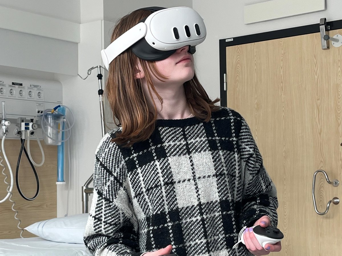 En flicka i tioårsåldern står med VR-headset och handkontroller i ett sjukhusrum.