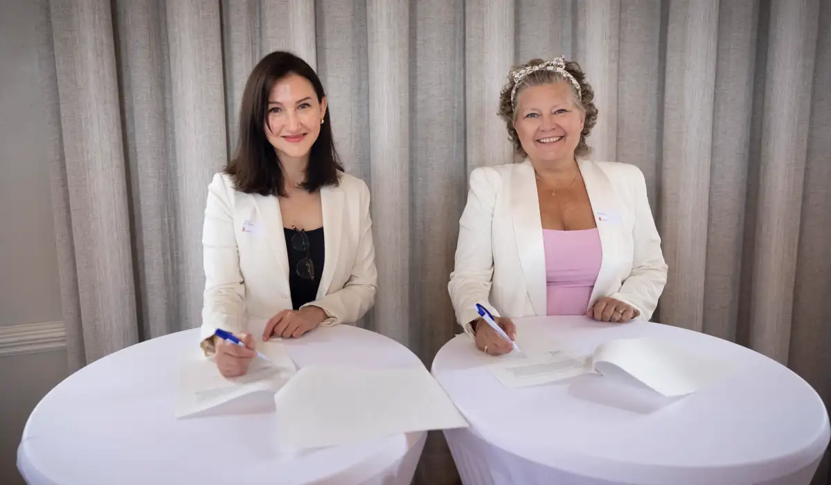Foto på Aida Hadžialić och Helena Proos som sitter vid ett bord och signerar avsiktsförklaringen. 