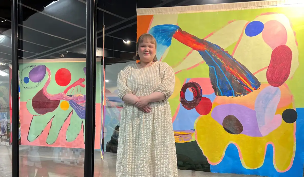 Linn står i montern framför två av målningarna i utställningen.
