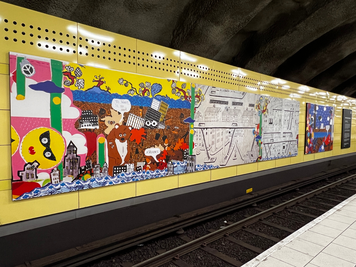 En tunnelbanestation med konsttavlor på en gul vägg.