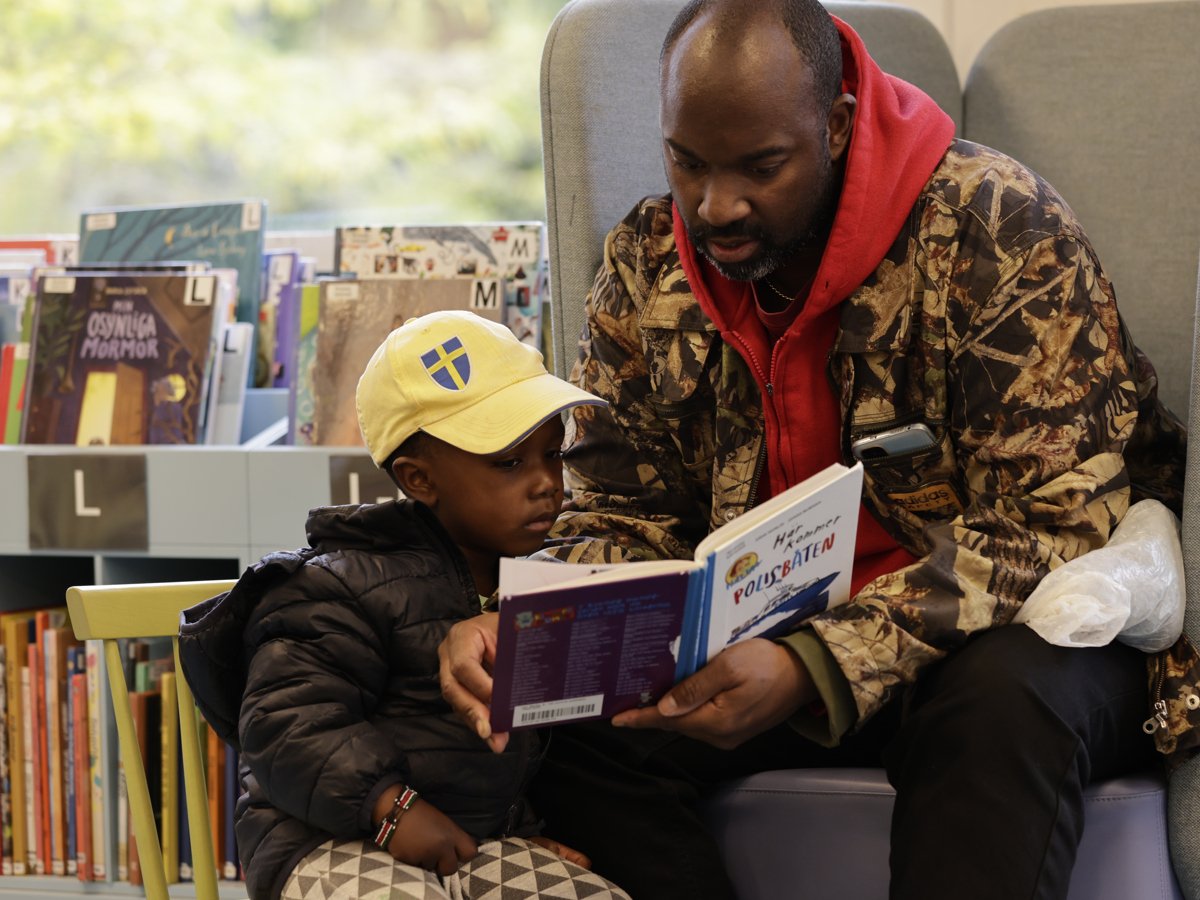 Pappa och son som läser en bok på biblioteket