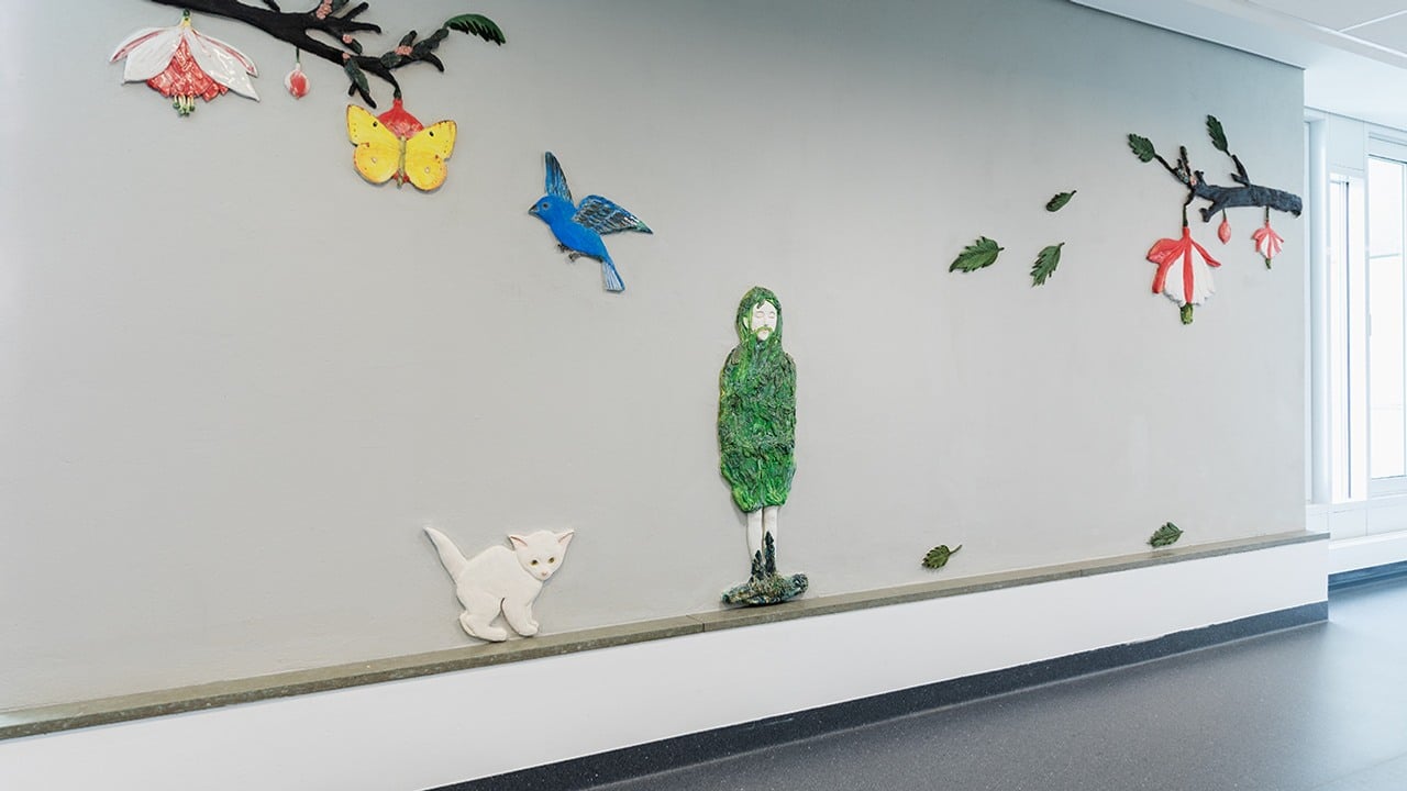 teckningslika keramikfigurer monterade på en vägg - en katt, en person och grenar med blad och blommor