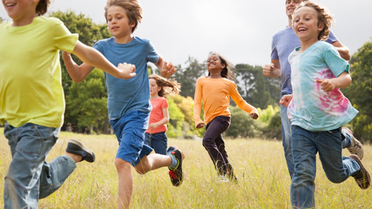 Barn, i åldern 9-10, springer på en äng tillsammans