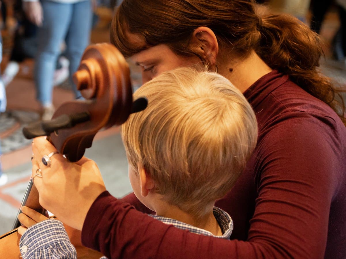 Ett barn får testa spela ett stråkinstrument med ledning av en musiker. 