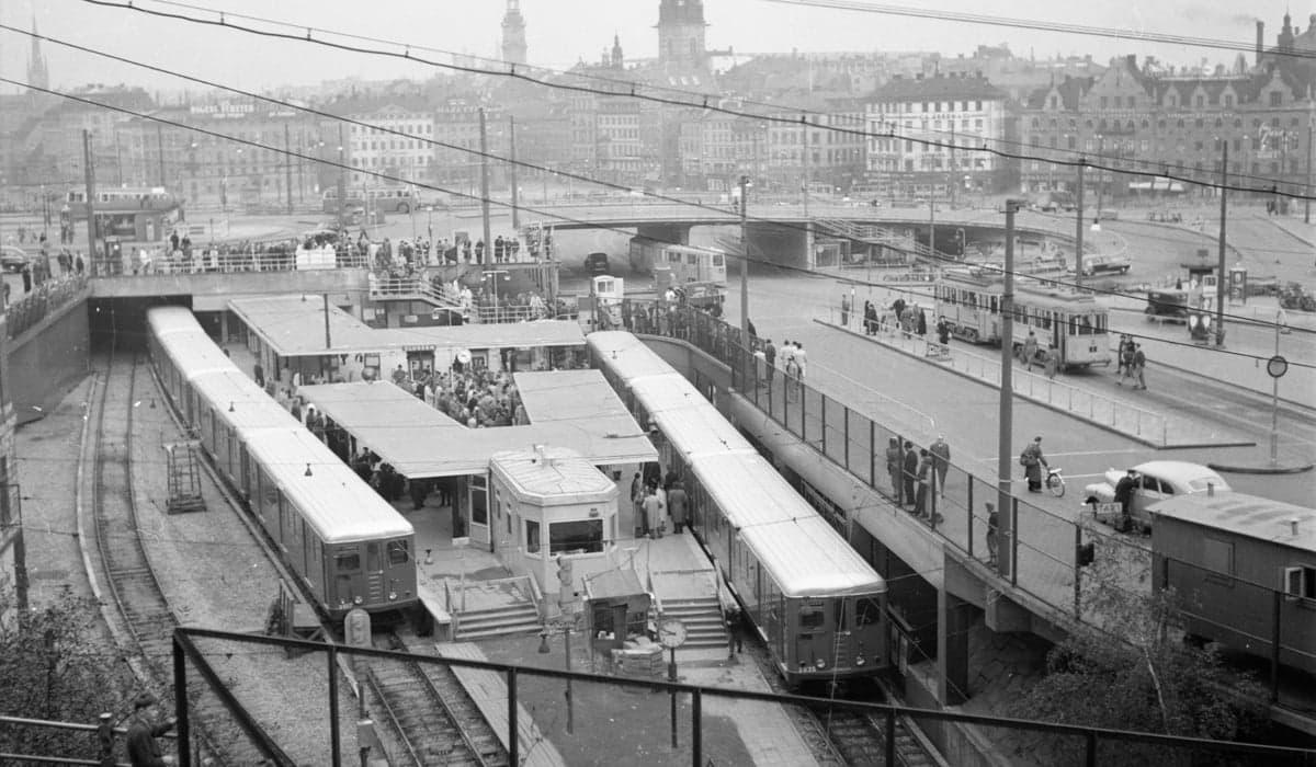 Slussen 1950 under invigningen. Två tåg står inne på plattformen, som är full av människor. Till höger av stationen finns byte till Spårvagn. I bakgrunden syns Gamla stan.