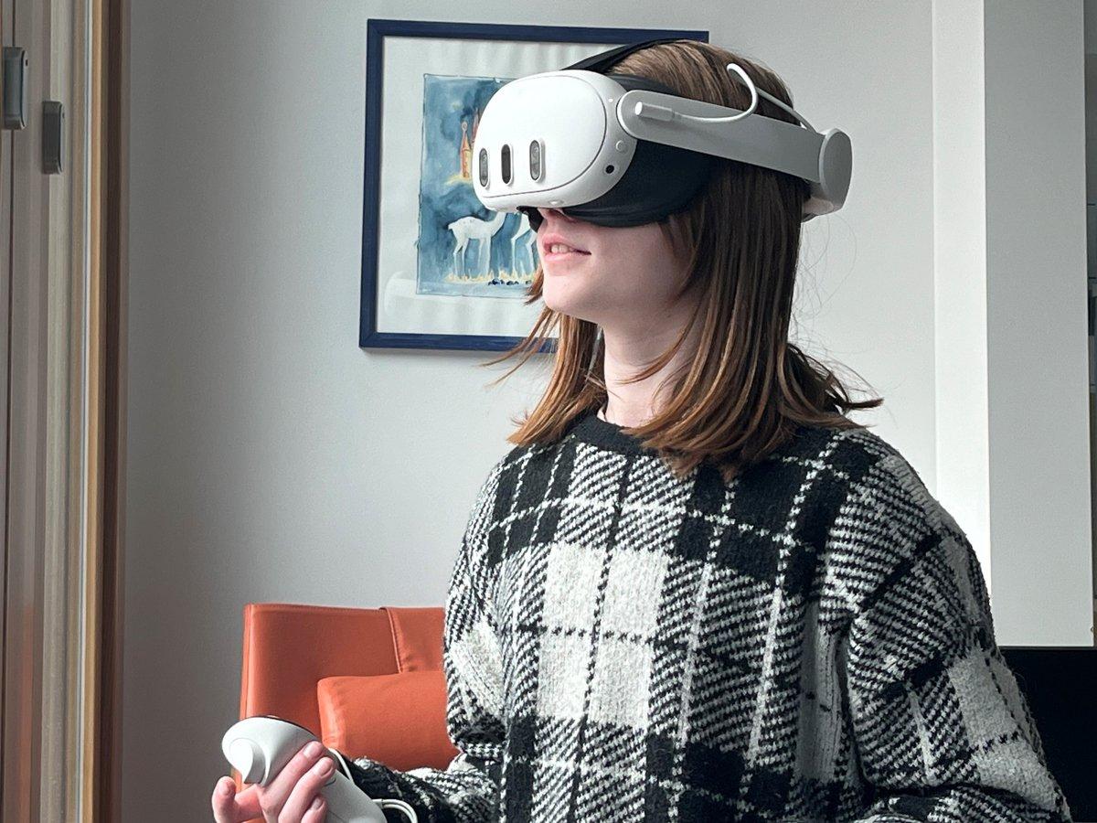 En flicka står med ett VR-headset på huvudet och med en handkontroll i ena handen i ett sjukhusrum. 