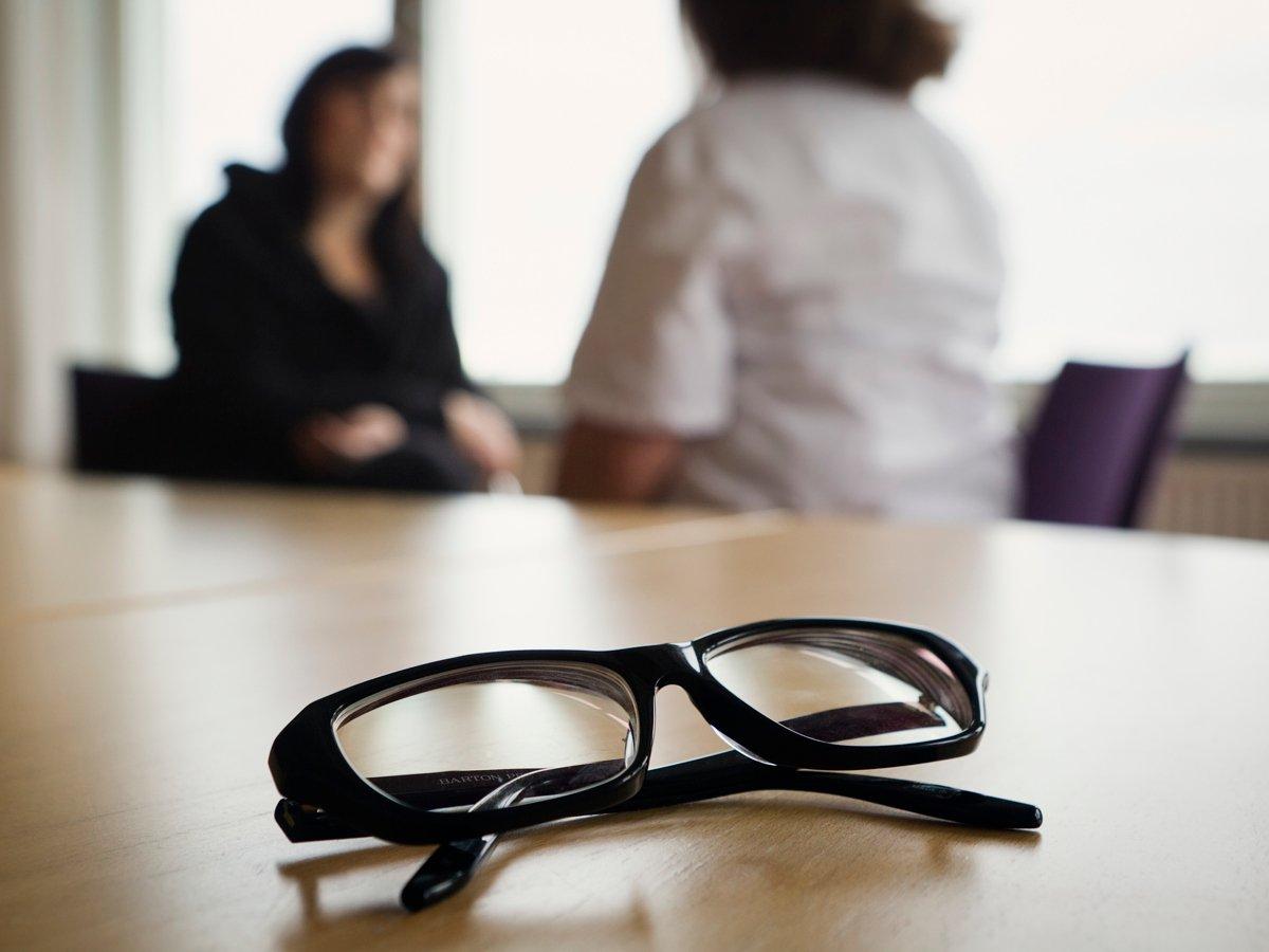 Foto på glasögon som ligger på ett bord. I bakgrunden syns två personer i oskärpa. 