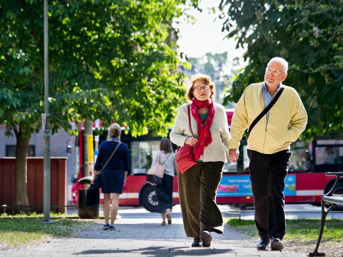 Äldre par som håller varandra i handen ute på promenad.