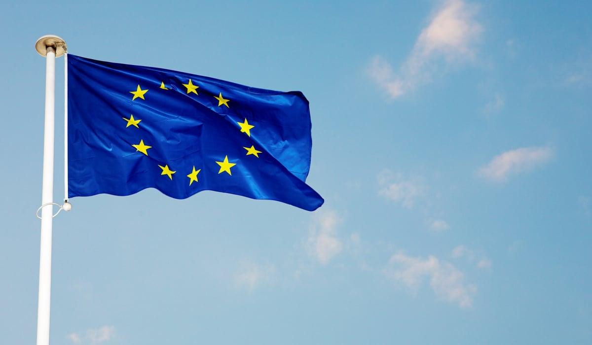 Bild på en blå EU-flagga som vajrar på en vit flaggstång med blå himmel i bakgrunden