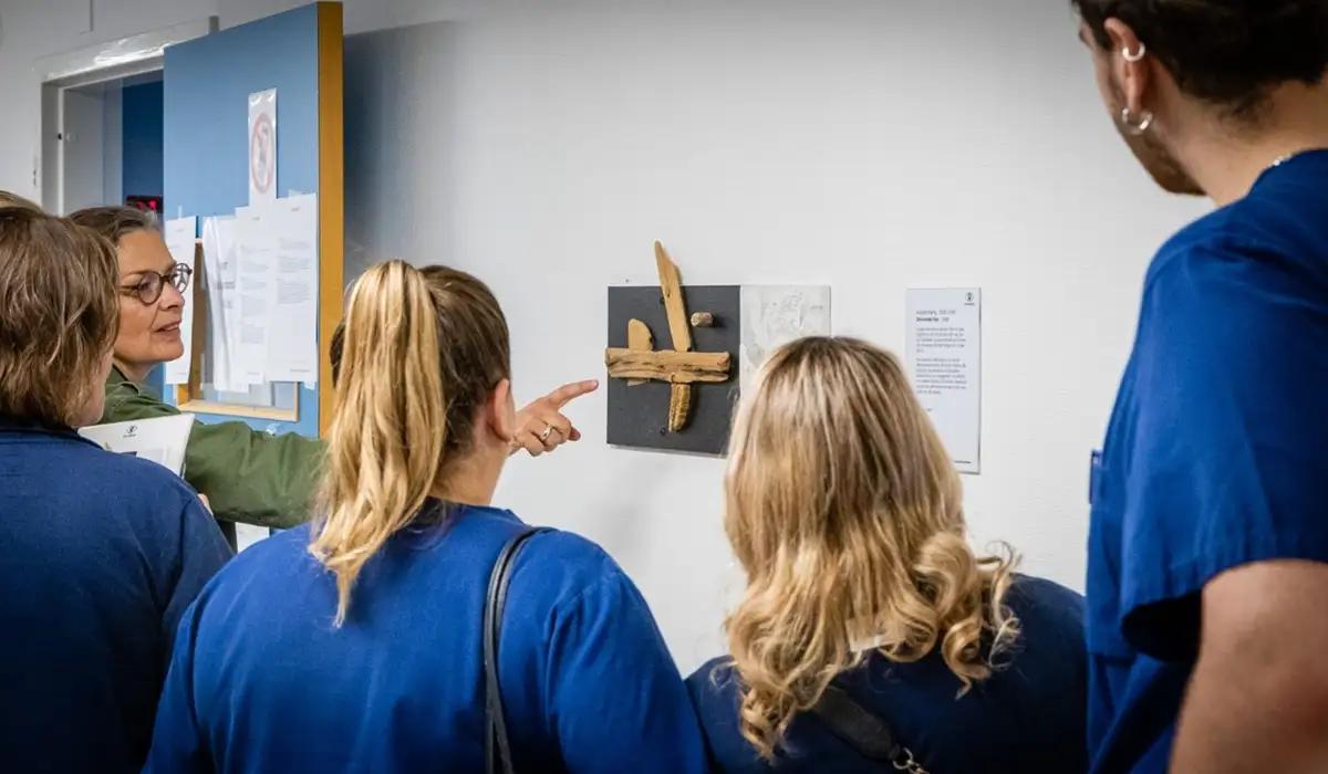 En grupp med personer vårdkläder tittar på en tavla på en vägg. En guide pekar på konstverket.