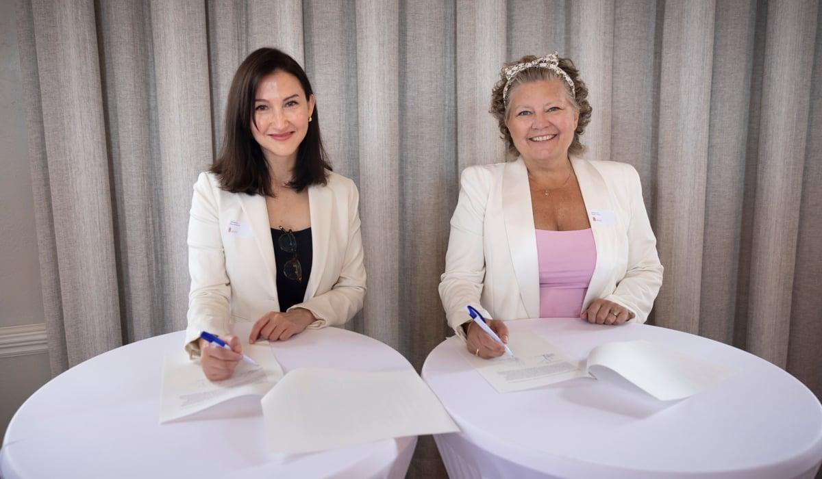 Foto på Aida Hadžialić och Helena Proos som sitter vid ett bord och signerar avsiktsförklaringen. 