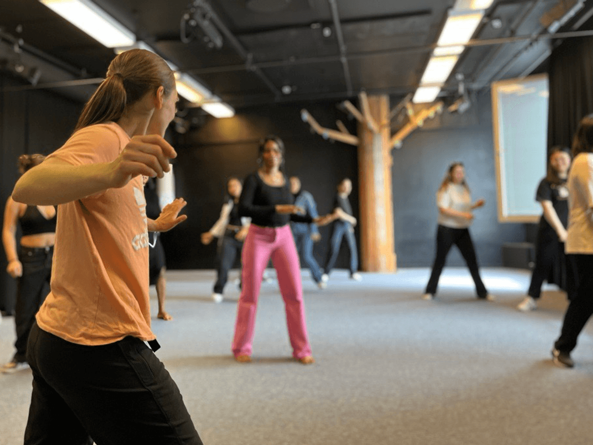 Dansinstruktör framför en grupp tjejer i träningskläder.
