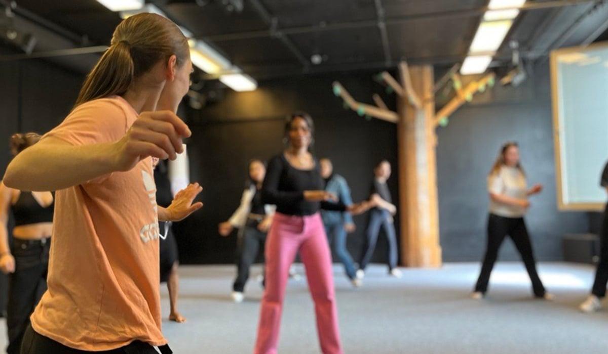 Dansinstruktör framför en grupp tjejer i träningskläder.