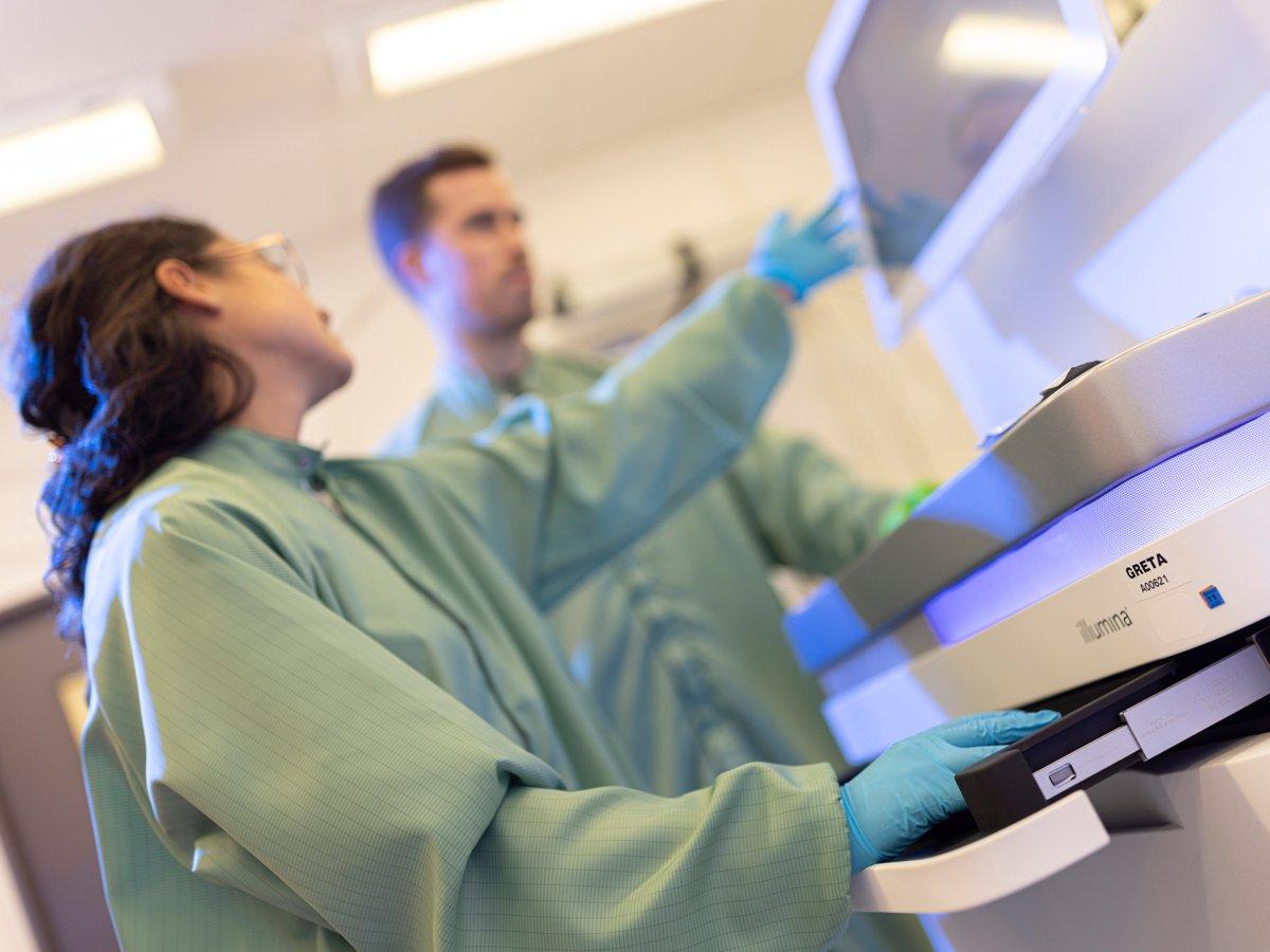 Två forskare i gröna rockar som står vid en maskin i ett laboratorium