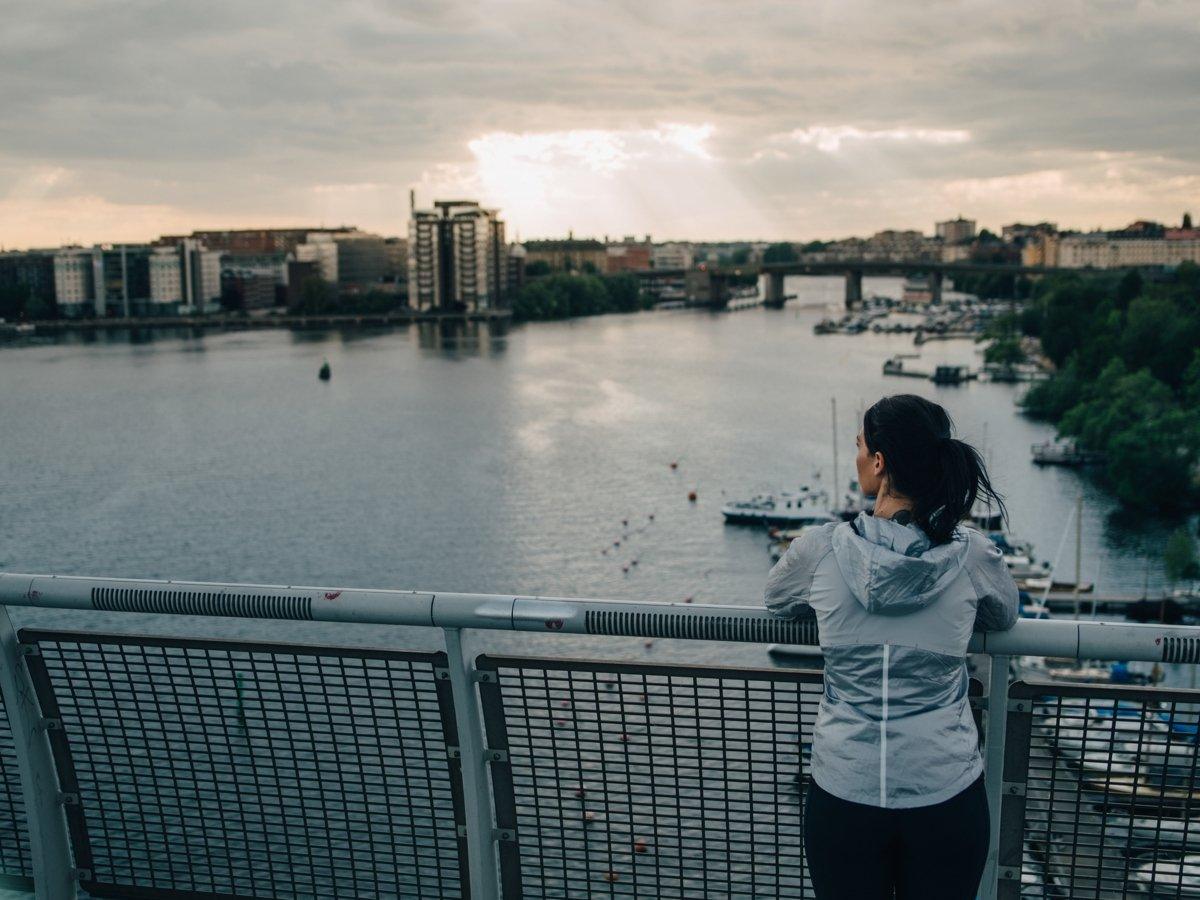 Kvinna stående på bro blickar ut över Stockholms vatten.