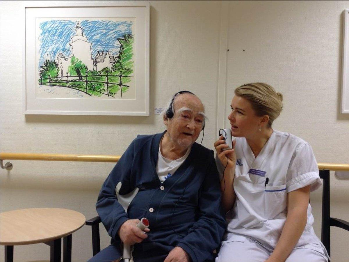 En äldre man och en sköterska sitter i en korridor och samtalar.