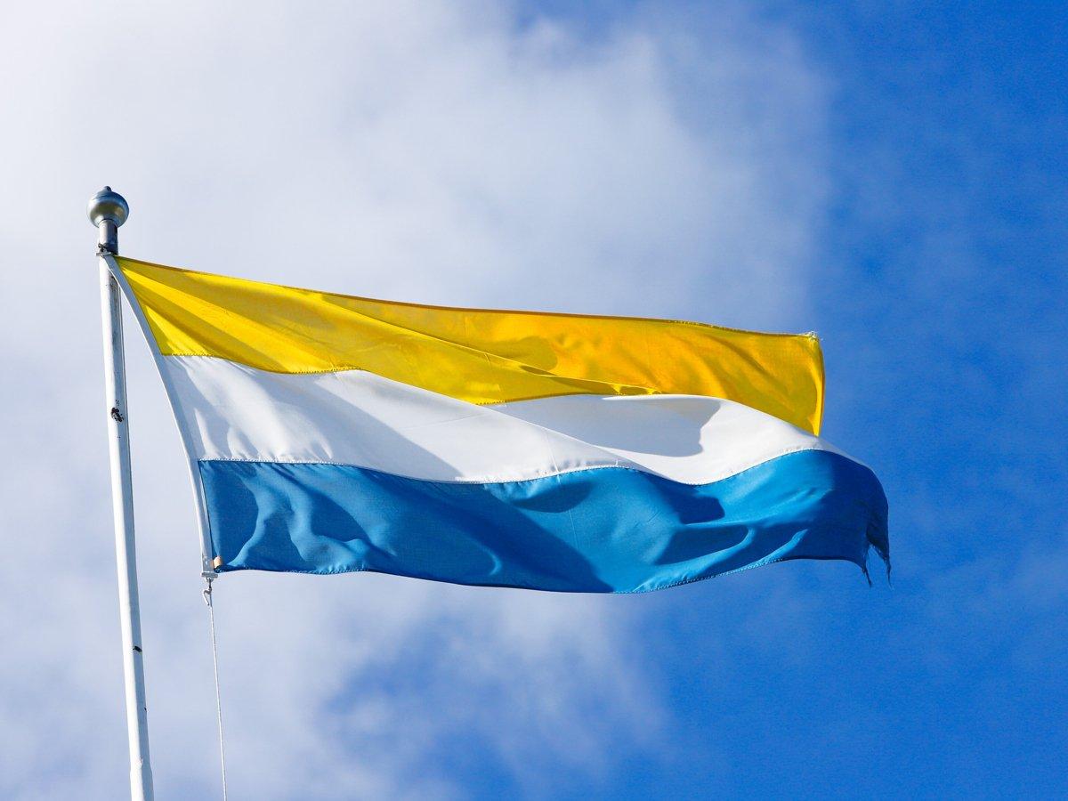 Tornedalens flagga, Meänflaku, vajar i vinden mot en blå himmel.