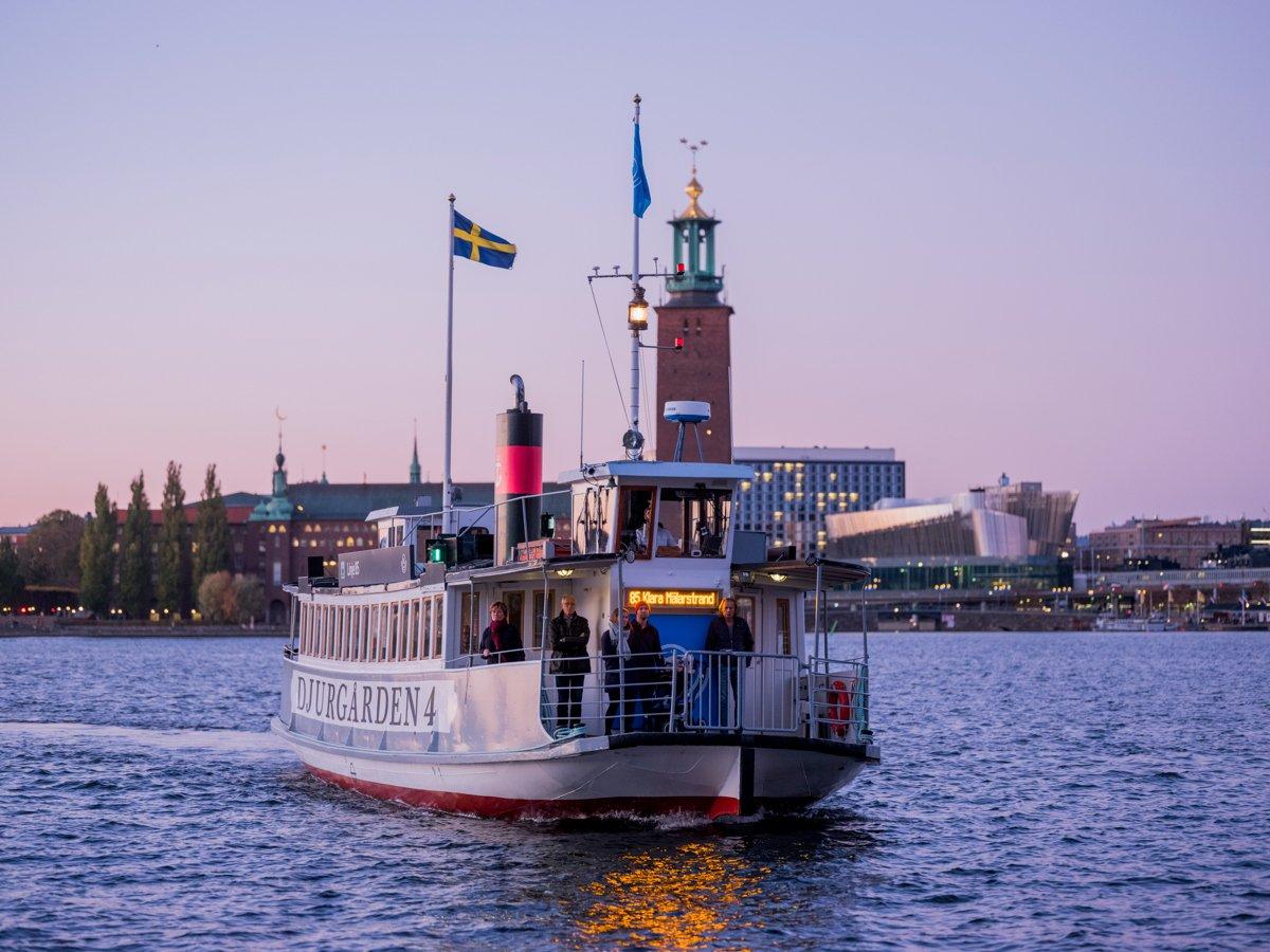 Pendelbåt som navigerar genom Stockholms innerstads vatten. Det är vinter och kyligt. Himmeln är lätt rosa.