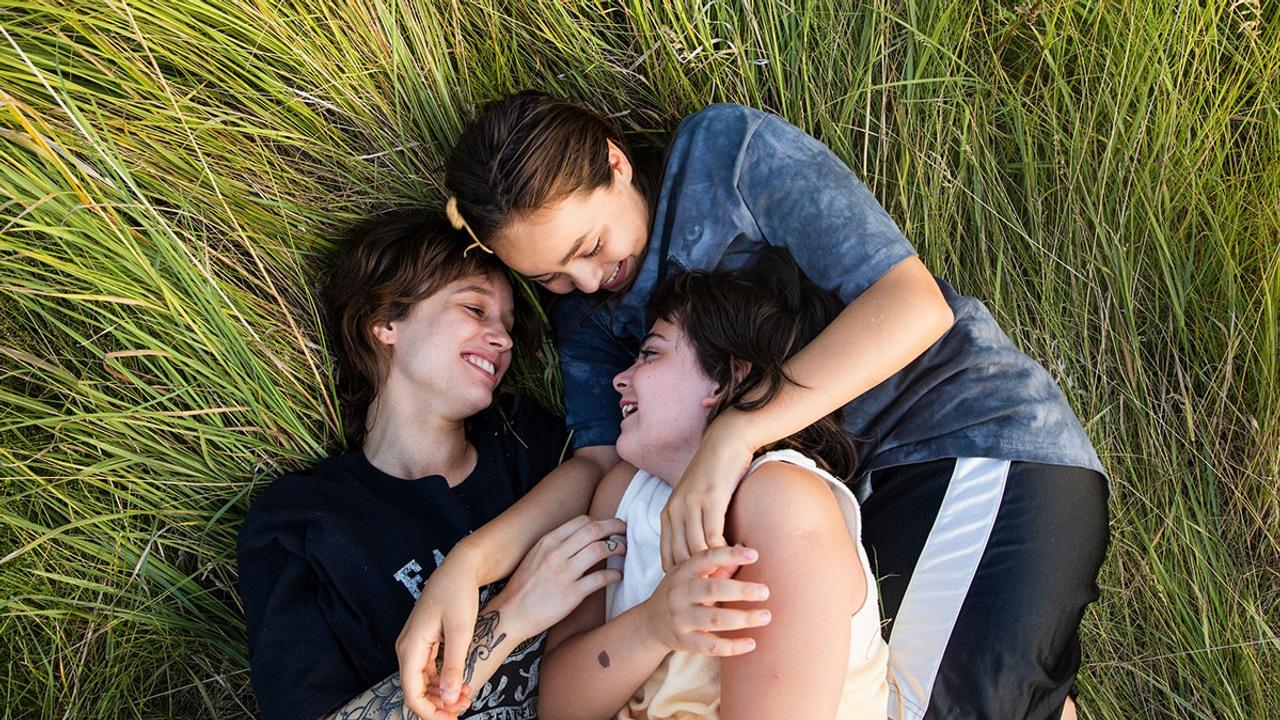 Tre personer ligger på ett gräsfält och skrattar