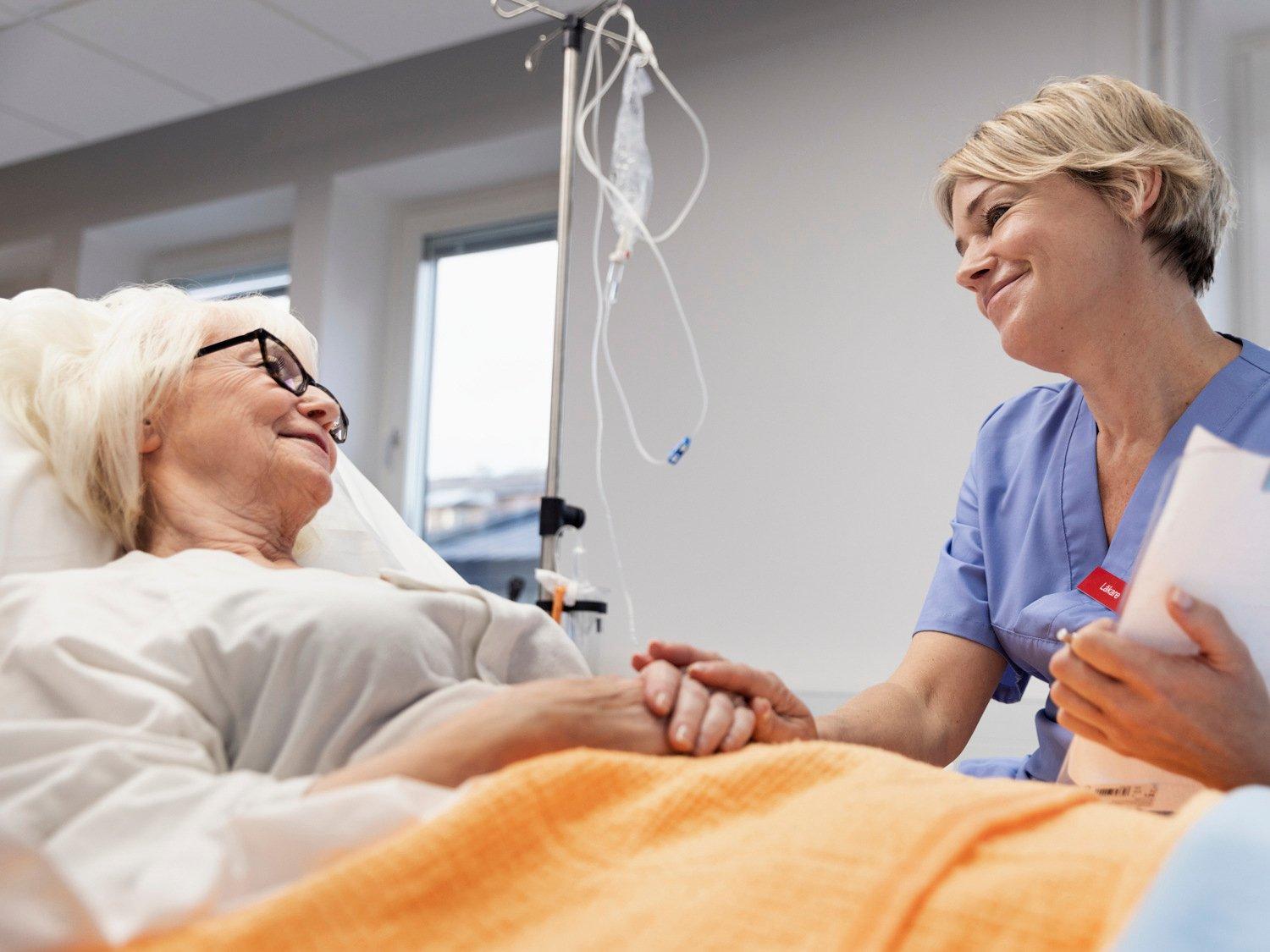 Läkare samtalar med äldre patient vid sin sjukhussäng 