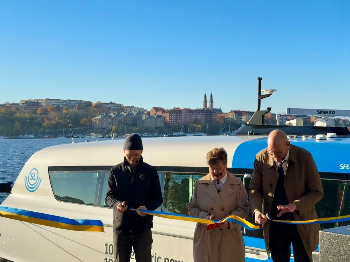 Niklas Nordin, produktchef på Candela, Charlott Andersson på strategisk utveckling på Trafikverket och Gustav Hemming, klimat- och infrastrukturregionråd klipper det blågula invigningsbandet för bärplansbåten Nova, som ligger förtöjd i bakgrunden vid Norr Mälarstrand.