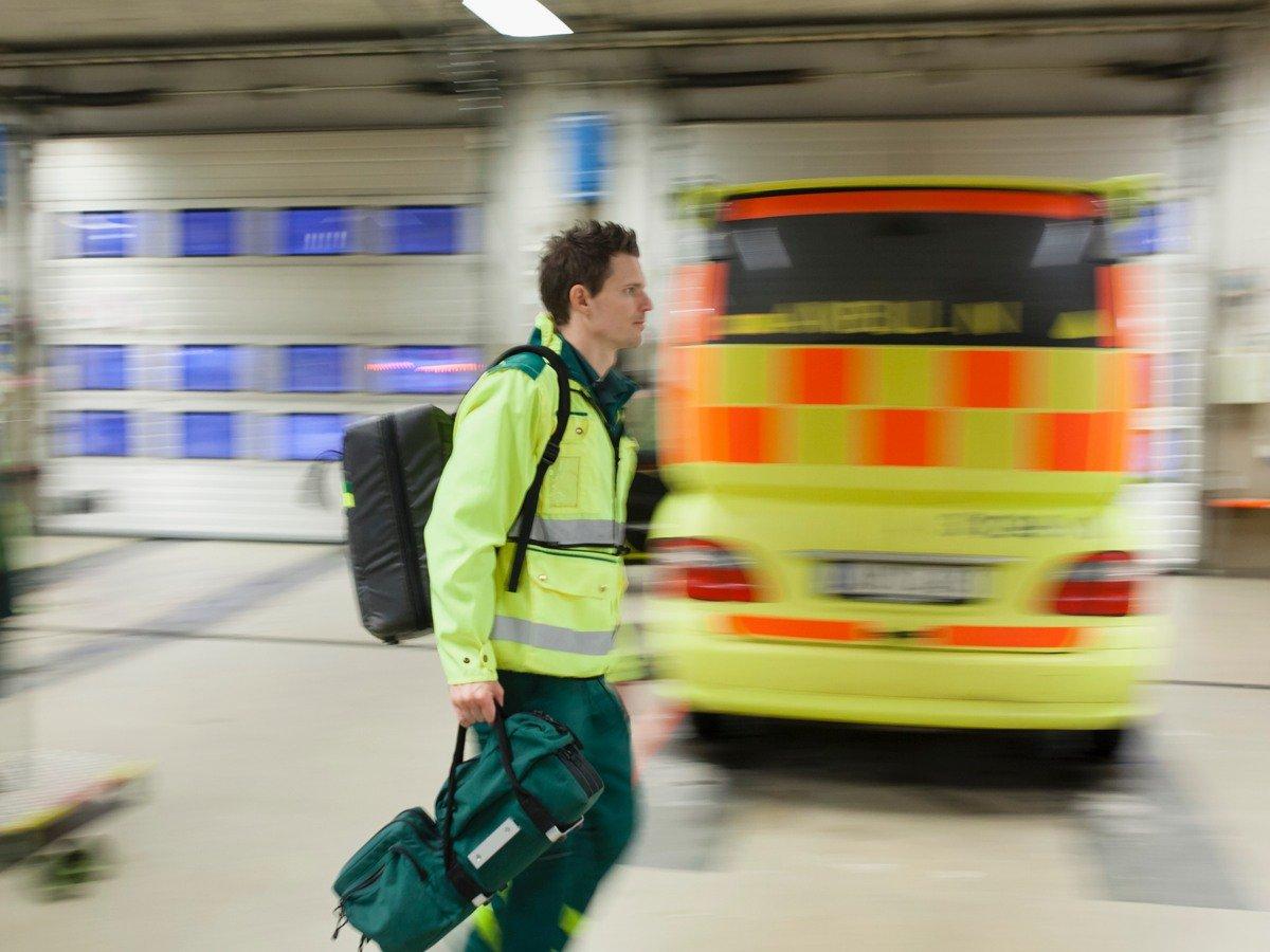 Ambulansförare som bär på utrustning och går förbi en stående ambulans inuti ett garage
