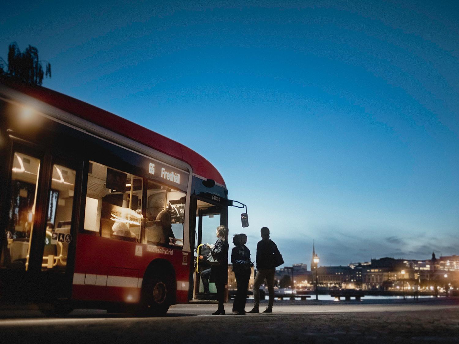 En rödbuss tar emot resenärer under skymning i Stockholm