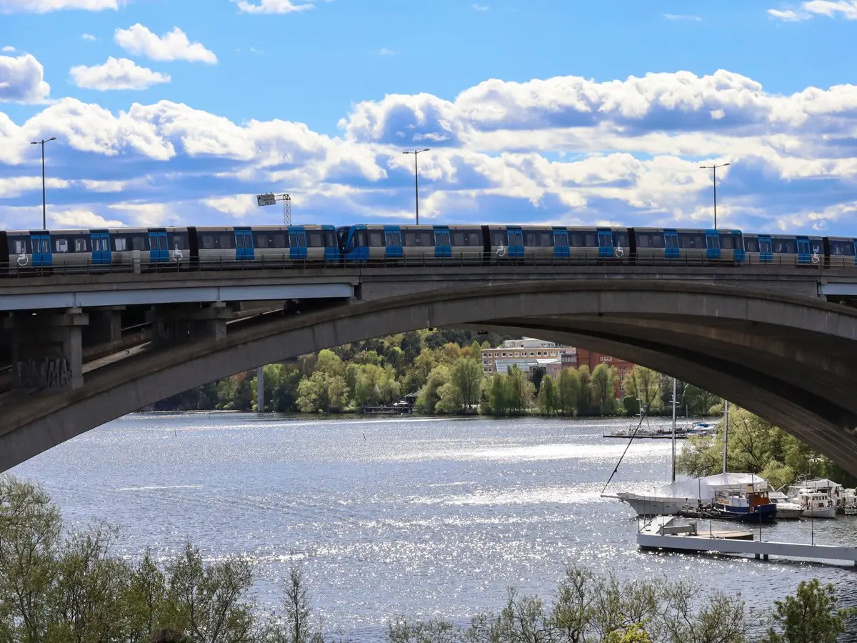 Bro över vatten. Tunnelbanetåg som åker över bron. Solig dag.