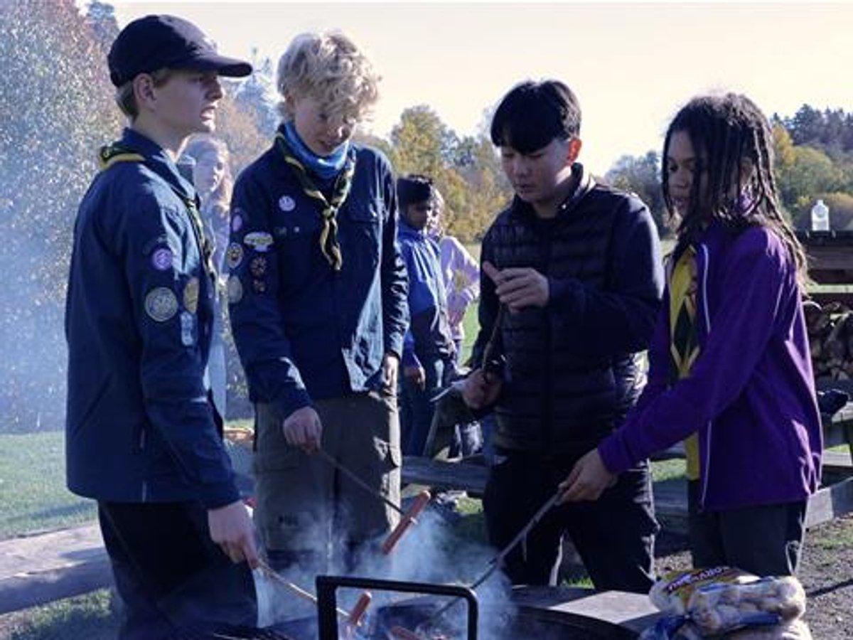 Fyra scouter står runt en eld och grillar korv,