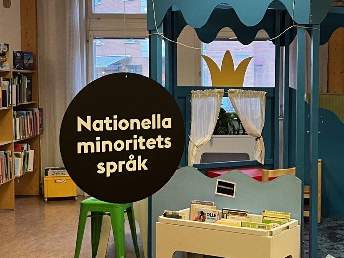 En svart rund skylt med texten nationella minoritetsspråk hänger på ett bibliotek