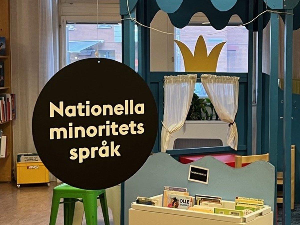 En svart rund skylt med texten nationella minoritetsspråk hänger på ett bibliotek