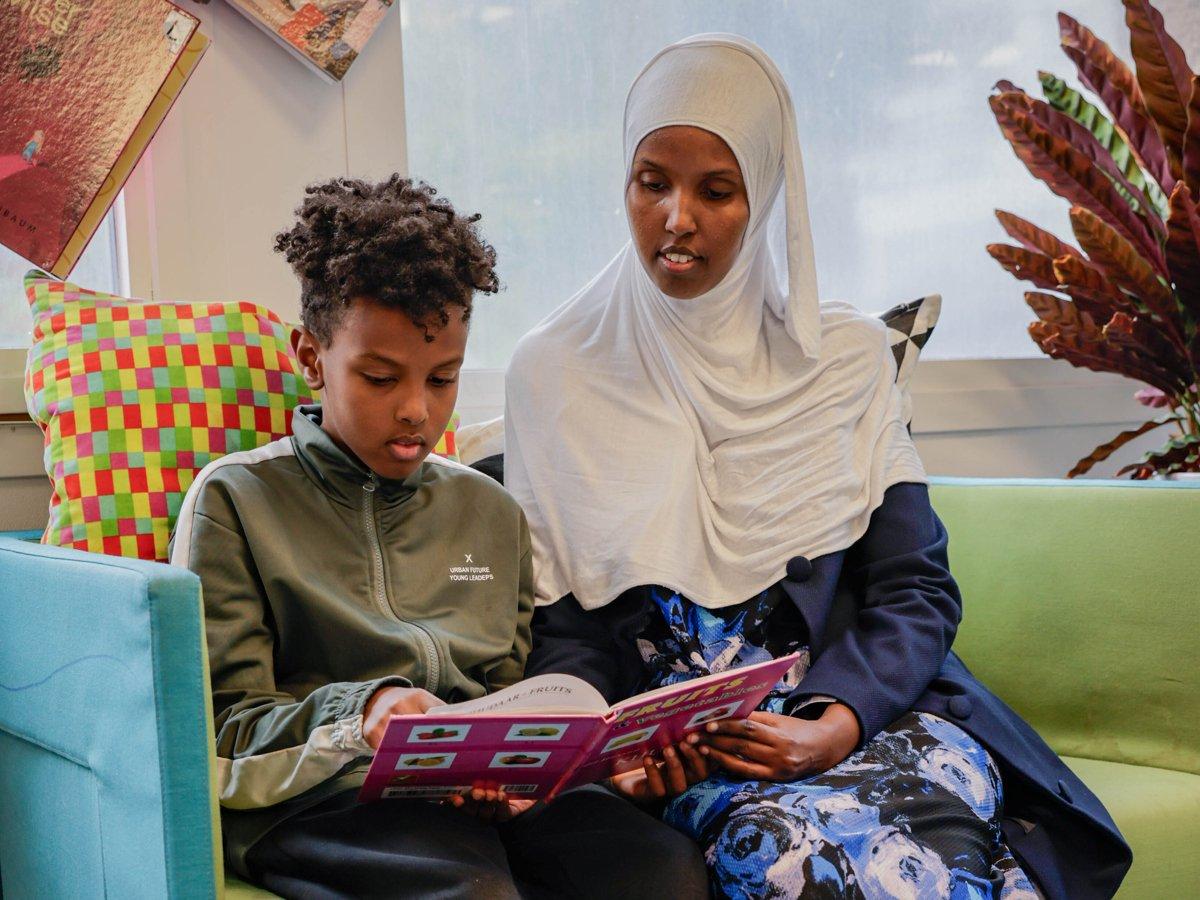 En mamma och hennes son sitter och läser en bok på ett bibliotek