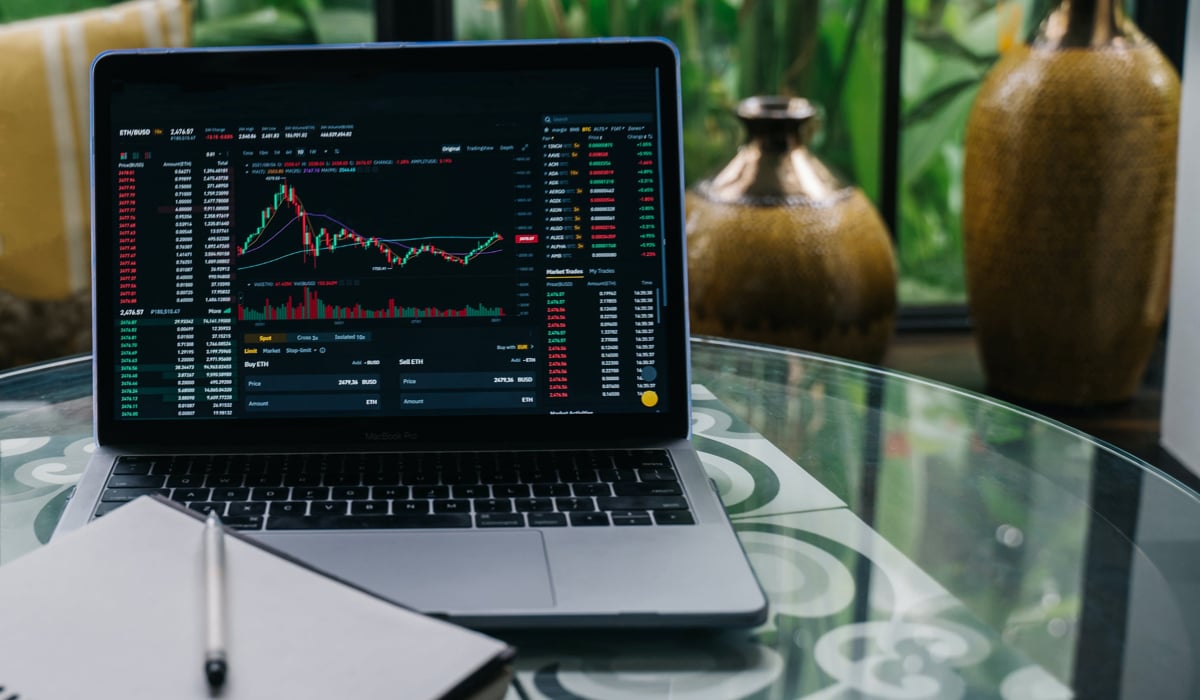 En dator som visar börsstatistik. Framför datorn finns en blädderblock och en vit penna.