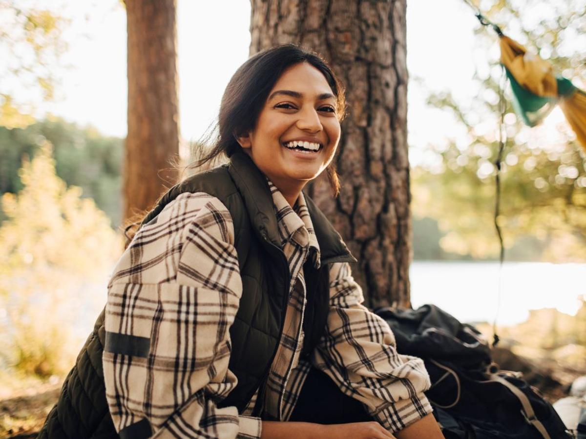 Foto på en kvinna som sitter i en skog. Hon ler in i kameran. 