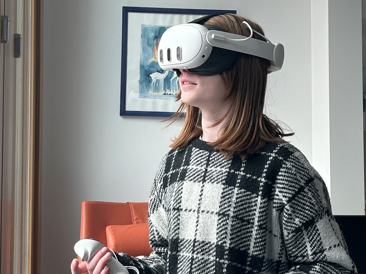 En flicka står med ett VR-headset på huvudet och med en handkontroll i ena handen i ett sjukhusrum.