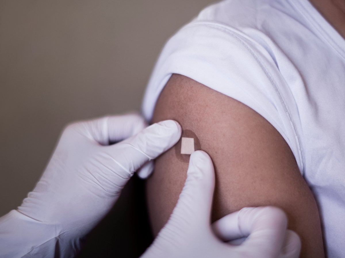 Bild på arm som precis fått en vaccinationsspruta. Vårdpersonal sätter på ett plåster på armen.