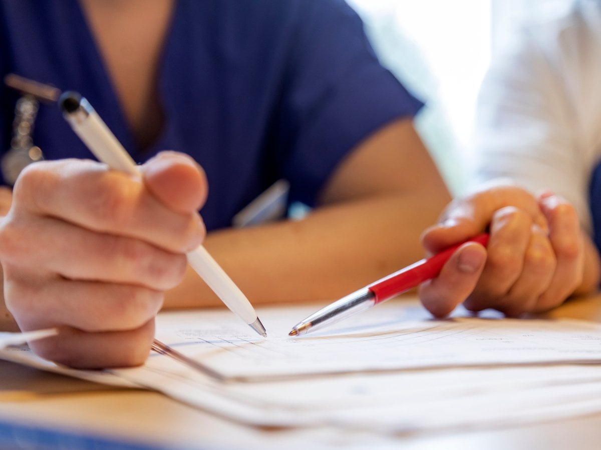 Närbild på två personer som håller i pennor och pekar på ett papper.