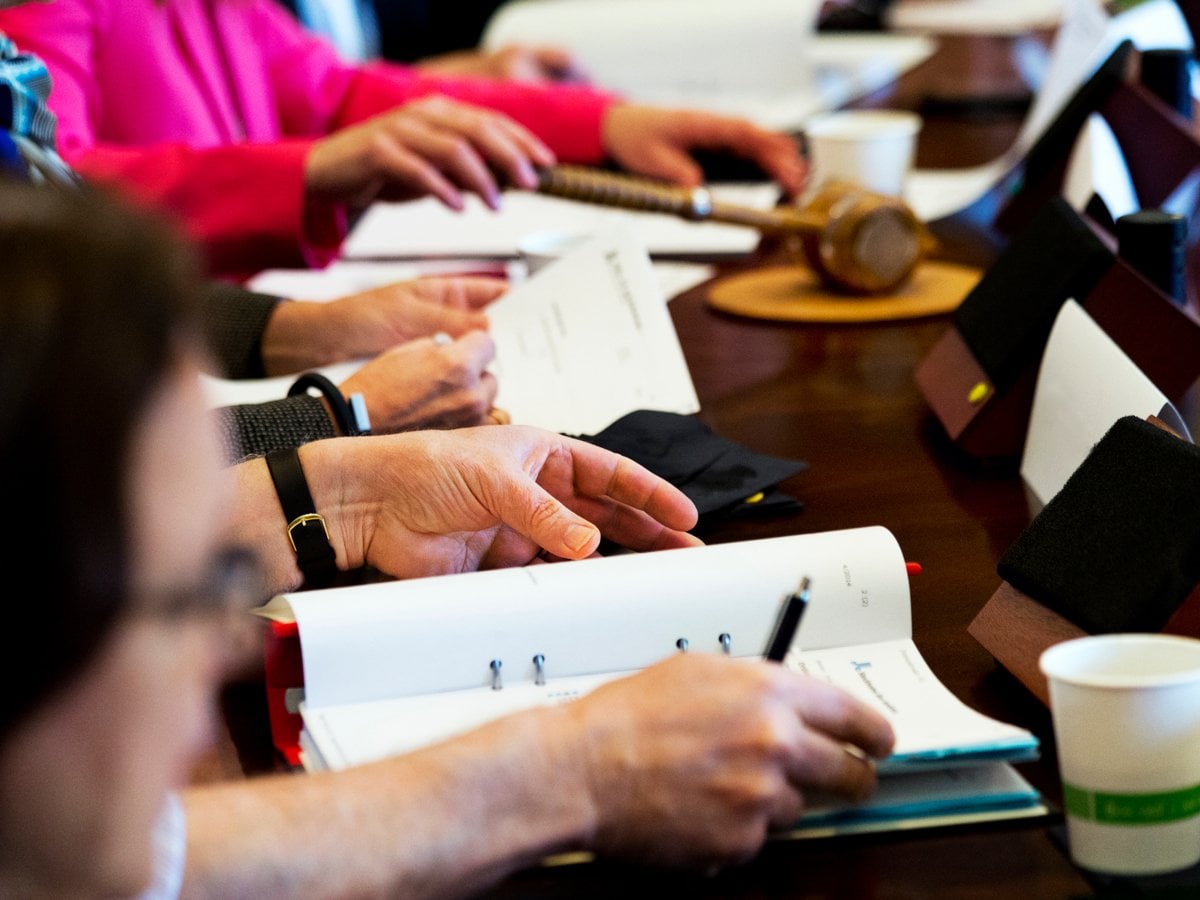 Bild på mötesbord. Mötesdeltagare läser ett underlag, i mitten av bordet en klubba som skvallrar om att det är där mötesordföranden sitter.