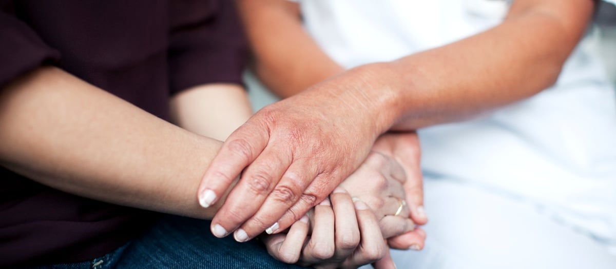 Vårdpersonals händer omfamnar patients händer.