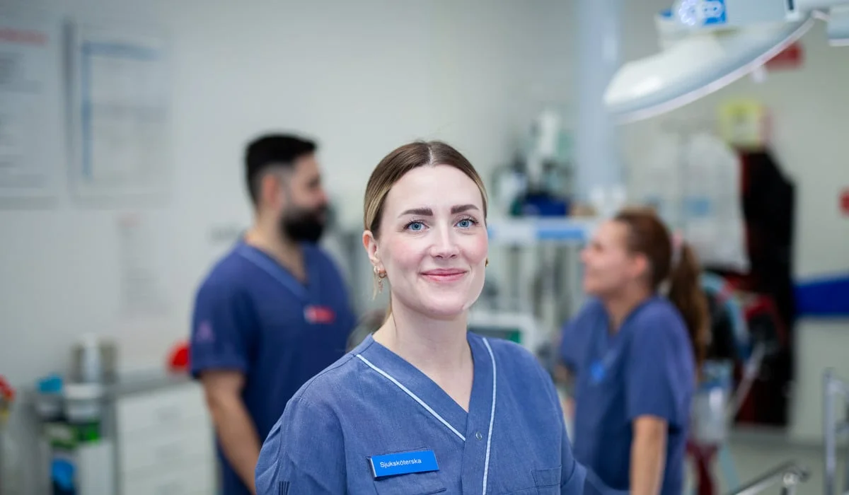 Leende sjuksköterska i förgrunden till en operationssal.